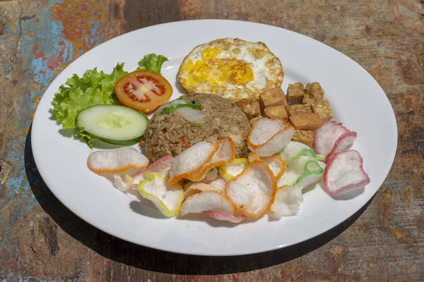 Sebzeli pilav, pirinç cipsi, peynirli tofu ve kızarmış yumurta yerel kafedeki eski ahşap masada, Endonezya mutfağını kapatın. Endonezya, Bali 'de Kahvaltı