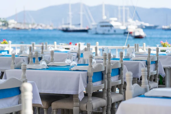 Elegant table setting with fork, knife, wine glass, white plate and blue napkin in restaurant. Nice dining table set with arranged silverware and napkin for dinner, Bodrum, Turkey. Beach cafe near sea