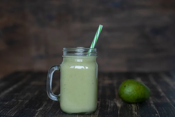 アボカド バナナ 蜂蜜をグラスマグカップに入れた新鮮な緑のスムージーを木製の背景に閉じます 健康的な食事の概念 — ストック写真