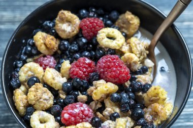 Siyah bir kasede ahududu, yaban mersini ve taneli müsli, yakın çekim. Sağlıklı yemek, sağlıklı kahvaltı konsepti