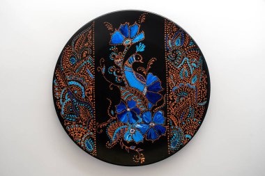 Çiçekli ve kuşlu dekoratif seramik tabak, beyaz arka planda boyalı, yakın plan, üst manzara. Akrilik boyalarla boyanmış dekoratif porselen tabaka, el işi, nokta boyası.