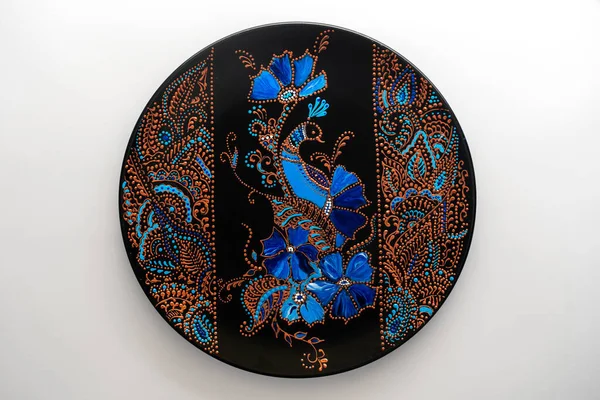 Çiçekli ve kuşlu dekoratif seramik tabak, beyaz arka planda boyalı, yakın plan, üst manzara. Akrilik boyalarla boyanmış dekoratif porselen tabaka, el işi, nokta boyası.