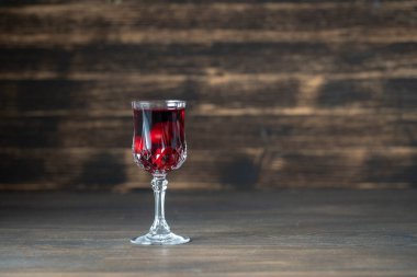 Ukrayna, ahşap zemin üzerinde şarap kristal bardağında ev yapımı kırmızı kiraz tentürü, yakın çekim, kopyalama alanı. Böğürtlen alkollü içki konsepti