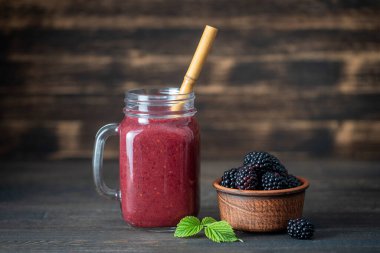 Ahşap arka plandaki cam kavanozda taze böğürtlen smoothie, yakın çekim. Sağlıklı gıda konsepti