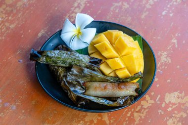 Tayland usulü tatlı, sarı mangolu ve palmiye yapraklı muzlu pilav. Sarı mango ve yapışkan pirinç Tayland 'ın popüler geleneksel tatlısıdır. Kapat.