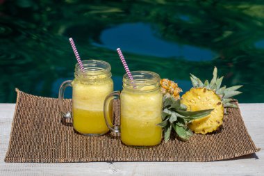 Ev yapımı mango ve hindistan cevizi sütüyle yapılmış ananas püresi yüzme havuzunun yanındaki cam bardakta, yakın plan. Endonezya, Bali Adası. Tropikal meyve içeceğini tazeliyorum. Sağlıklı beslenme kavramı.