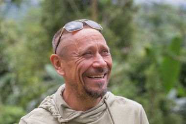 İnsanlar ve yaşam tarzı konsepti. Yeşil doğa geçmişine karşı orta yaşlı, traşsız, mutlu bir adam. Yetişkin adam portresi. Yakından.