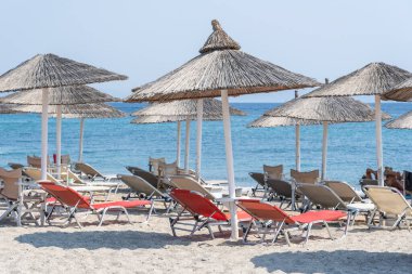 Sahildeki deniz suyunda güneş yatakları ve şemsiyeler, Yunanistan