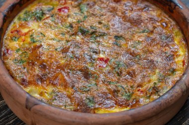 Sebzeli frittata ile seramik kase, basit vejetaryen yemeği. Tahta masada domates, biber, soğan ve peynirli frittata, yakın çekim. İtalyan omleti, üst manzara.