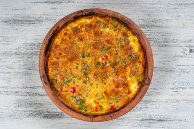 Sebzeli frittata ile seramik kase, basit vejetaryen yemeği. Tahta masada domates, biber, soğan ve peynirli frittata, yakın çekim. İtalyan omleti, üst manzara.