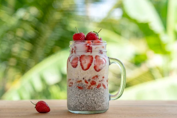 Almond milk chia pudding with fresh red strawberries, goji berries and oat flakes in a glass jar mug. Vegan raw breakfast. Chia seeds and fresh cut fruits and berries dessert, close up