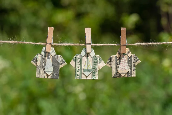 Asılı yeşil doğa üzerine dolar banknotundan yapılmış Origami gömleği. İpe asılmış dolar banknotları. Kapatın. Dolar Tişörtü