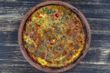 Sebzeli frittata ile seramik kase, basit vejetaryen yemeği. Tahta masada domates, biber, soğan ve peynirli frittata, yakın çekim. İtalyan omleti, üst manzara.