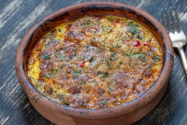 Sebzeli frittata ile seramik kase, basit vejetaryen yemeği. Tahta masada domates, biber, soğan ve peynirli frittata, yakın çekim. İtalyan omleti, üst manzara.