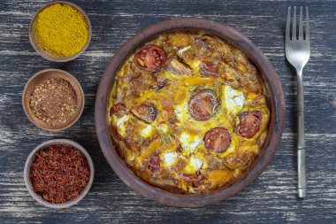 Sebzeli frittata ile seramik kase, basit vejetaryen yemeği. Tahta masada domates, biber, soğan ve peynirli frittata, yakın çekim. İtalyan omleti, üst manzara.