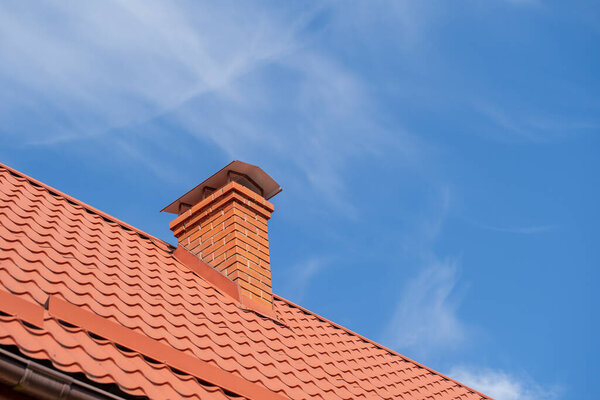 Red roof of a detached house and chimney against the blue sky, close up