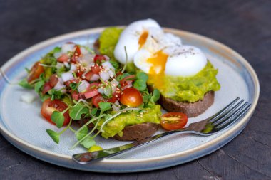 Ekmek tostlu sağlıklı kahvaltı ve yeşil salatalı haşlanmış yumurta, kırmızı domates ve tabakta ezilmiş avokado, yakın çekim.