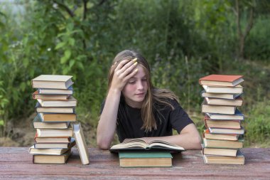 Bahçede, tahta bir masada kitap yığınıyla kitap okuyan genç bir kız. Ev eğitimi kavramı