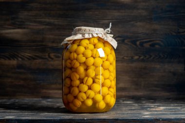 Ev yapımı kiraz eriği konservesi. Berry alkollü içecekler konsepti. Ahşap zemin üzerinde cam kavanozda olgunlaşmış kiraz eriğinden yapılmış ev yapımı sarı şarap, Ukrayna
