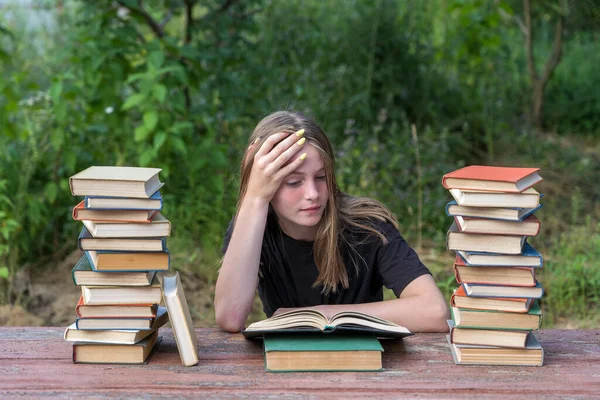 Bahçede, tahta bir masada kitap yığınıyla kitap okuyan genç bir kız. Ev eğitimi kavramı