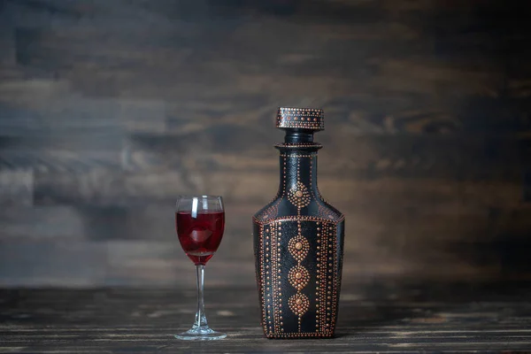 Homemade tincture of red cherry in a decorative bottles and a wineglass on wooden background, Ukraine, close up