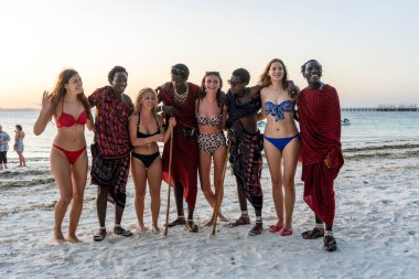Zanzibar, Tanzanya - 31 Aralık 2019: Avrupalı bir kızla birlikte Afrikalı erkekler, Doğu Afrika 'daki Tanzanya' nın Zanzibar adasındaki okyanus kıyısındaki tropikal plajda fotoğraf çekiyorlar