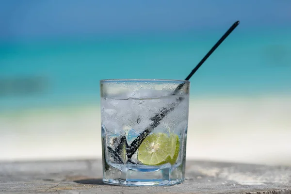 Soda water with lime and ice on a wooden table near the sea on the beach, close up
