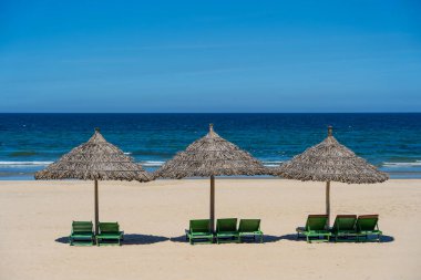 Danang şehrinde tropik kum plajı ve mavi gökyüzü ve üç saman şemsiyeli yaz denizi suyu. Seyahat ve doğa kavramı