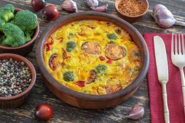 Sebzeli frittata ile seramik kase, basit vejetaryen yemeği. Yumurta, domates, biber, soğan, brokoli ve peynirli frittata, ahşap masaya, yakın çekim. İtalyan omleti.