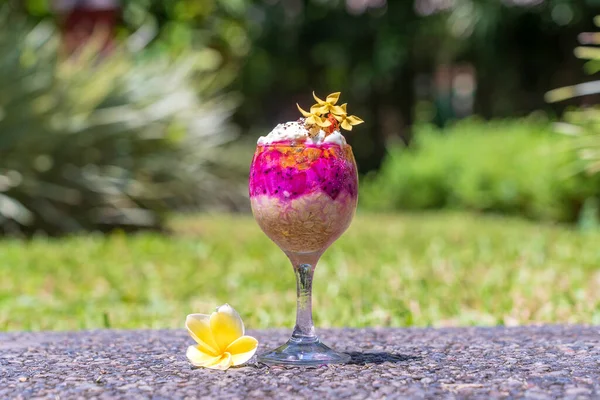 Fruit breakfast in a glass of oatmeal, red dragon fruit, passion fruit, mango and honey in nature background, close up. The concept of healthy eating.