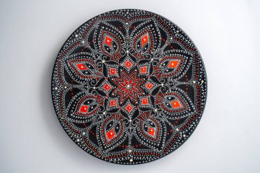 Kırmızı ve gümüş renkli dekoratif seramik tabak, beyaz arka planda boyanmış plaka, yakın plan, üst manzara. Akrilik boyalarla boyanmış dekoratif porselen tabaka, el işi, nokta boyası.