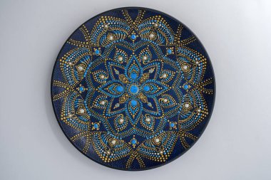 Dekoratif seramik plaka, siyah, mavi ve altın renkli, beyaz arka planda boyalı, yakın plan, üst manzara. Akrilik boyalarla boyanmış dekoratif porselen tabaka, el işi, nokta boyası.