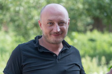 Kameraya bakan orta yaşlı, beyaz, kel bir adamın yakın çekimi. İnsanlar ve yaşam tarzı konsepti. Doğada, açık havada orta yaşlı bir adamın portresi.