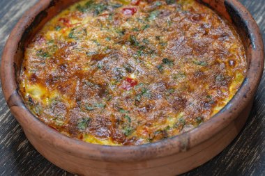Sebzeli frittata ile seramik kase, basit vejetaryen yemeği. Tahta masada domates, biber, soğan ve peynirli frittata, yakın çekim. İtalyan omleti, üst manzara.