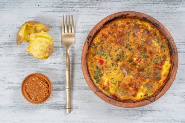 Sebzeli frittata ile seramik kase, basit vejetaryen yemeği. Tahta masada domates, biber, soğan ve peynirli frittata, yakın çekim. İtalyan omleti, üst manzara.