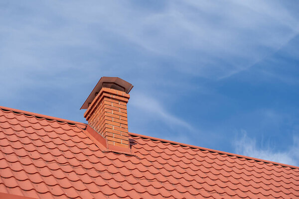 Red roof of a detached house and chimney against the blue sky, close up
