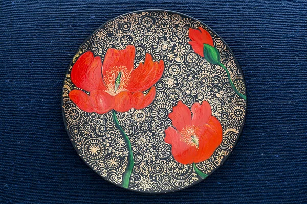 Decorative ceramic plate with red poppies, painted plate on a blue fabric background, close-up, top view. Decorative porcelain plate painted with acrylic paints, handwork, dot painting