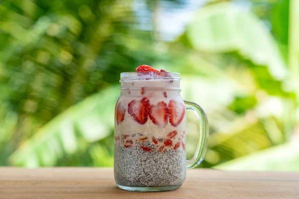 Almond milk chia pudding with fresh red strawberries, goji berries and oat flakes in a glass jar mug. Vegan raw breakfast. Chia seeds and fresh cut fruits and berries dessert, close up