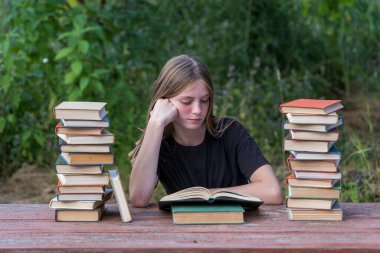 Bahçede, tahta bir masada kitap yığınıyla kitap okuyan genç bir kız. Ev eğitimi kavramı