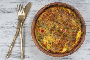 Sebzeli frittata ile seramik kase, basit vejetaryen yemeği. Tahta masada domates, biber, soğan ve peynirli frittata, yakın çekim. İtalyan omleti, üst manzara.