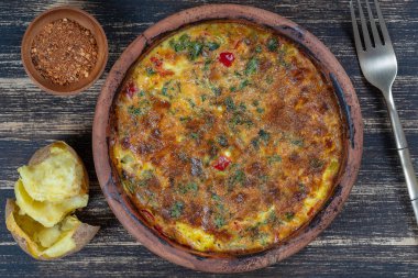 Sebzeli frittata ile seramik kase, basit vejetaryen yemeği. Tahta masada domates, biber, soğan ve peynirli frittata, yakın çekim. İtalyan omleti, üst manzara.