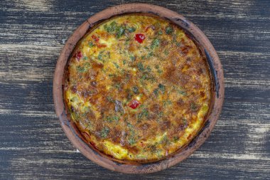 Sebzeli frittata ile seramik kase, basit vejetaryen yemeği. Tahta masada domates, biber, soğan ve peynirli frittata, yakın çekim. İtalyan omleti, üst manzara.
