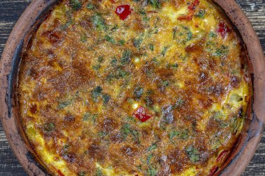 Sebzeli frittata ile seramik kase, basit vejetaryen yemeği. Tahta masada domates, biber, soğan ve peynirli frittata, yakın çekim. İtalyan omleti, üst manzara.