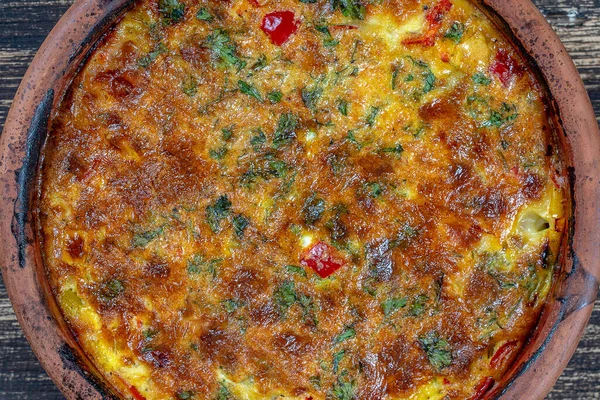 Sebzeli frittata ile seramik kase, basit vejetaryen yemeği. Tahta masada domates, biber, soğan ve peynirli frittata, yakın çekim. İtalyan omleti, üst manzara.