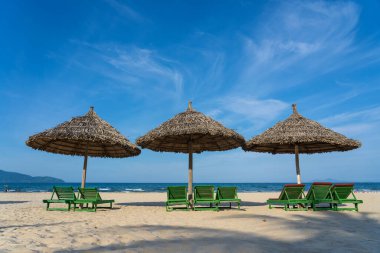 Danang şehrinde tropik kum plajı ve mavi gökyüzü ve üç saman şemsiyeli yaz denizi suyu. Seyahat ve doğa kavramı