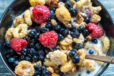Siyah bir kasede ahududu, yaban mersini ve taneli müsli, yakın çekim. Sağlıklı yemek, sağlıklı kahvaltı konsepti