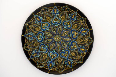 Dekoratif seramik plaka, siyah, mavi ve altın renkli, beyaz arka planda boyalı, yakın plan, üst manzara. Akrilik boyalarla boyanmış dekoratif porselen tabaka, el işi, nokta boyası.