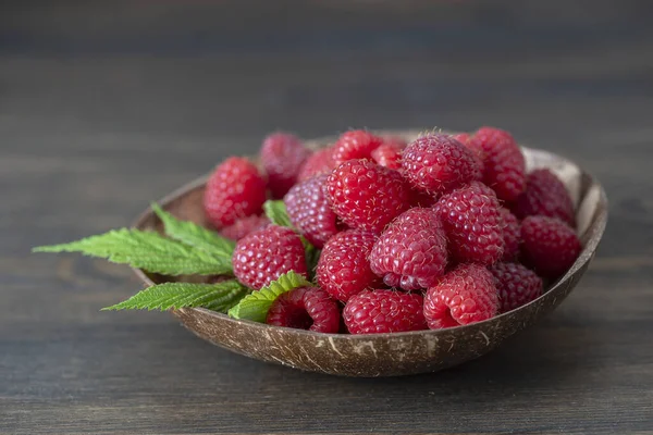 Kahverengi ahşap arka planda, hindistan cevizi tabağında kırmızı ahududu hasadı. Kapat.