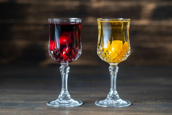 Homemade tincture of red cherry and yellow cherry plum in a wine crystal glasses on wooden background, Ukraine, close up. Berry alcoholic drinks concept