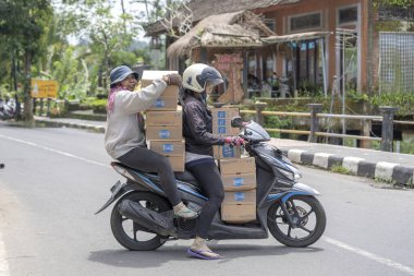 UBUD, BALI, INDONEZYA - 24 Mart 2019: Tanımlanamayan iki kadın, Ubud, Bali, Endonezya 'da bir sokakta motosikletle mal taşıyor.